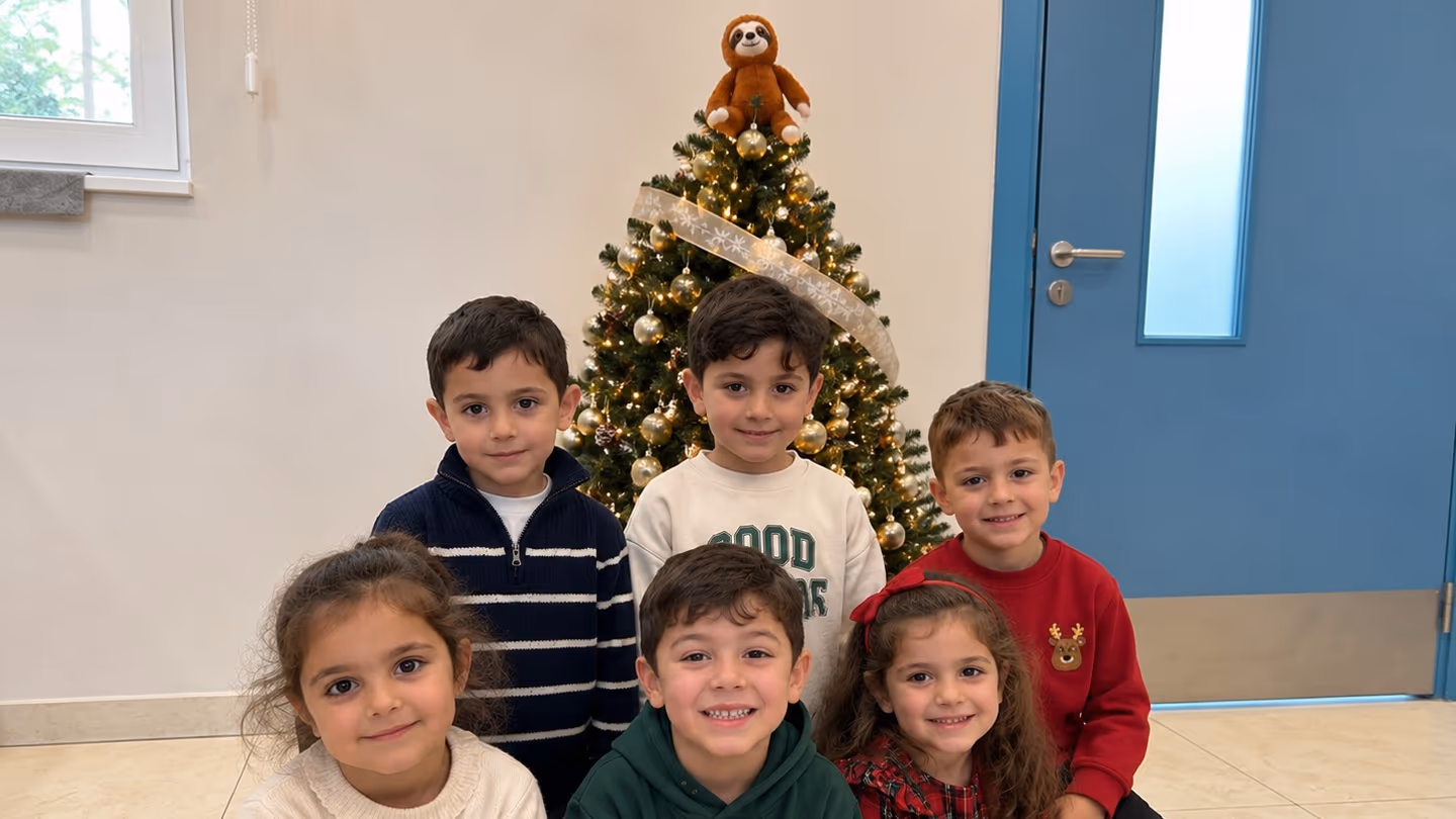 Six children smiling together in front of a Christmas tree topped with a toy sloth at a Camp Willingness camp